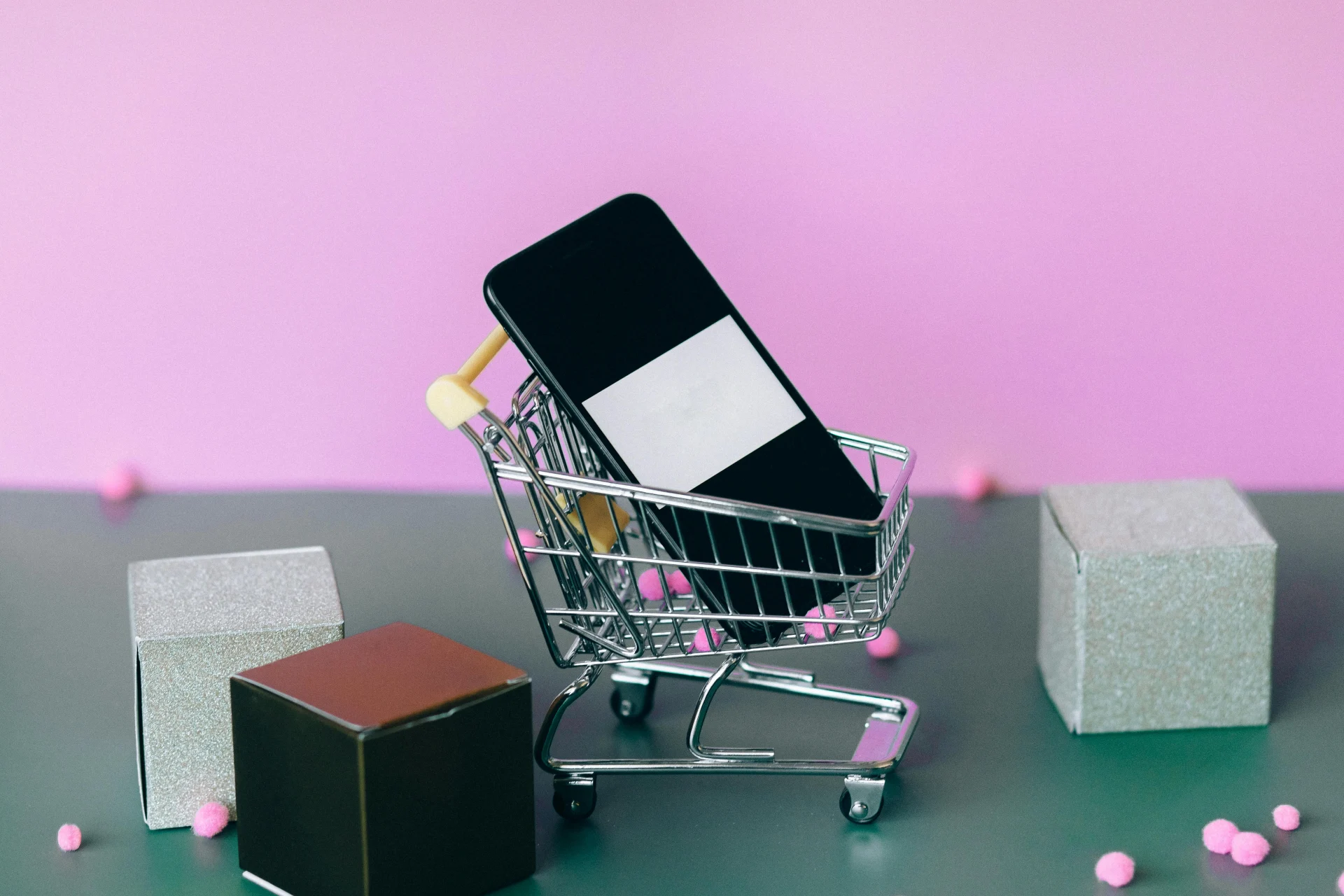 Smartphone inside mini shopping cart, decorative boxes.
